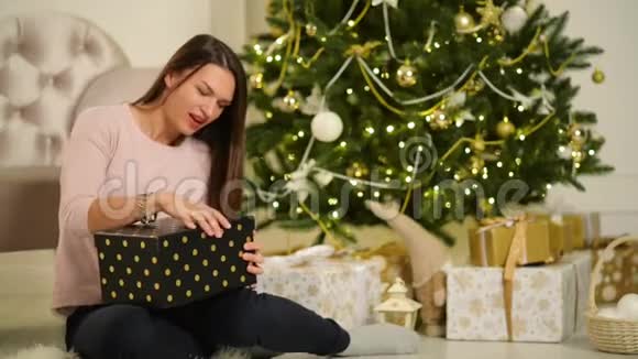 美丽的幸福女人坐在圣诞树旁边手里拿着礼物圣诞快乐新年理念视频的预览图