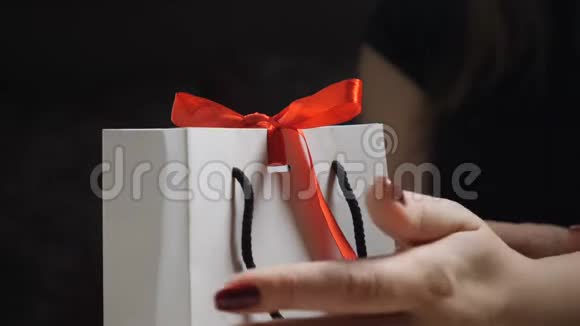 暗影女性手指的特写展示了带有红色丝带和蝴蝶结的纸礼盒打开一个礼物视频的预览图