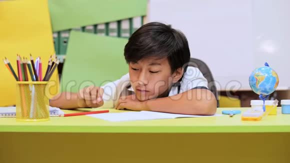 一个男孩懒洋洋地坐在桌子旁拿着铅笔在笔记本上写了一些东西视频的预览图