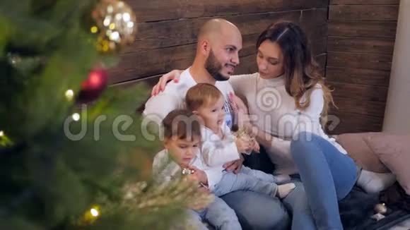 一家人无所事事年轻的父母和孩子在圣诞节早上坐在靠近圣诞树的房间里视频的预览图