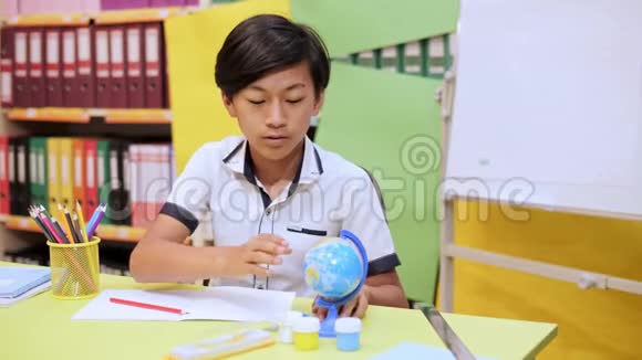 一个坐在桌子旁的男孩把地球扭曲在笔记本上写字视频的预览图