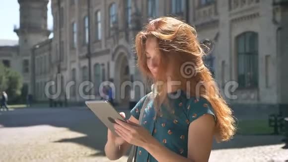 美丽的姜女在平板电脑上打字风吹乱了她的头发站在街上微笑快乐和快乐视频的预览图
