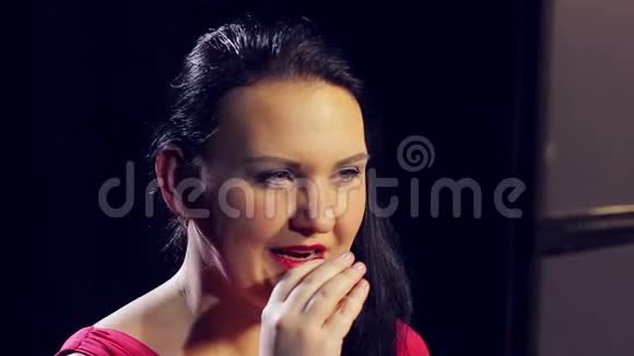 一个年轻的黑发女人穿着红色的裙子用鲜红的口红在嘴唇上涂上颜色视频的预览图