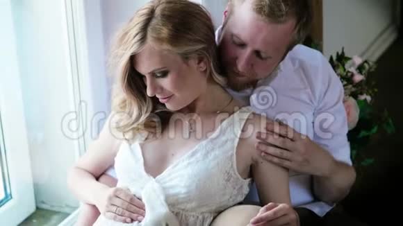 她丈夫旁边穿着白色连衣裙的孕妇正坐在地板上幸福的家庭期待着孩子丈夫视频的预览图