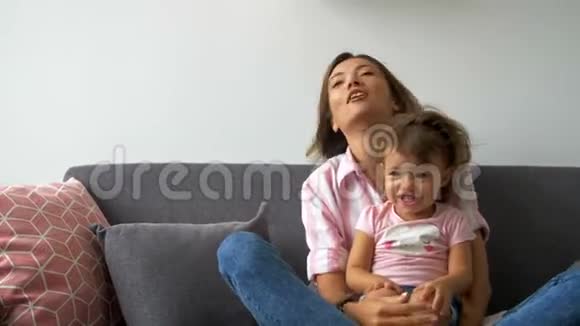 幸福美丽有爱的家庭年轻的母亲和女儿坐在沙发上笑着微笑的母亲和孩子玩得开心视频的预览图