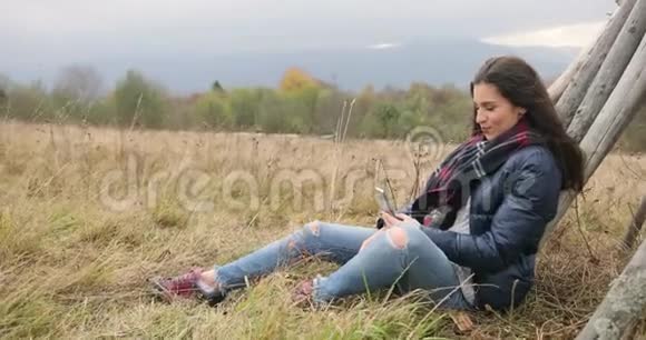山地休闲秋天的歌声漂亮的黑发女人穿着牛仔裤和皮夹克坐在山上看上去很漂亮视频的预览图