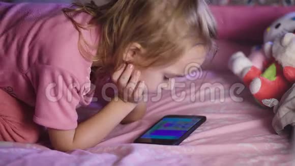 美丽的孩子金发穿着粉红色的衬衫躺在婴儿床上看着妈妈手机上的卡通女孩视频的预览图
