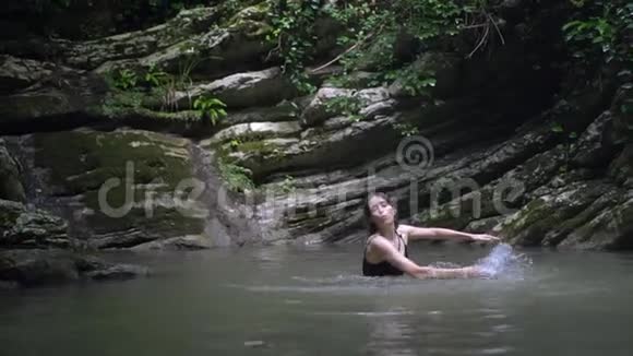 慢动作年轻快乐的女人用手泼在水上在绿色热带森林的小山湖里玩得开心视频的预览图