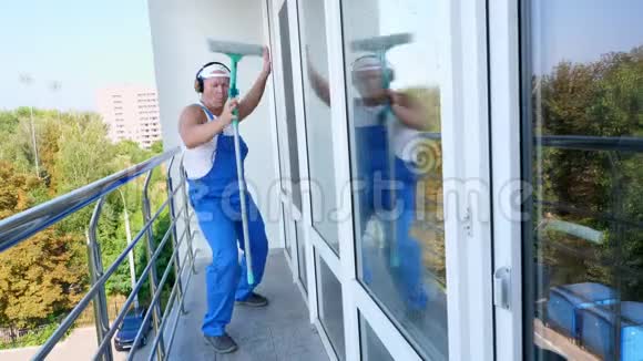 白人魅力男子清洁服务工人穿着带耳机的蓝色工作服玩得开心跳舞继续玩视频的预览图
