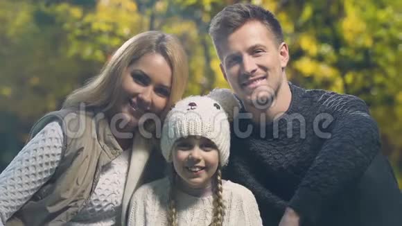 幸福的年轻家庭和美丽的女儿在秋天的森林里摆着相机视频的预览图