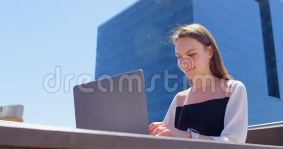 年轻的酷白种人女商人在现代化办公室的阳台上用笔记本电脑工作的正面景色视频的预览图