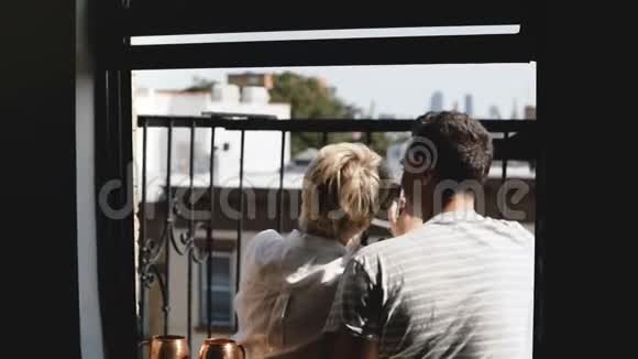 后景幸福年轻夫妇坐在阳光明媚的纽约小公寓阳台上拍智能手机自拍视频的预览图