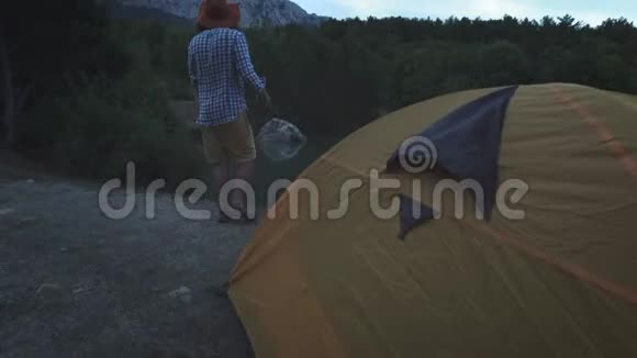 一个年轻的徒步旅行者站在帐篷附近湖边大型森林蜘蛛积极的生活方式穿着格子衬衫视频的预览图
