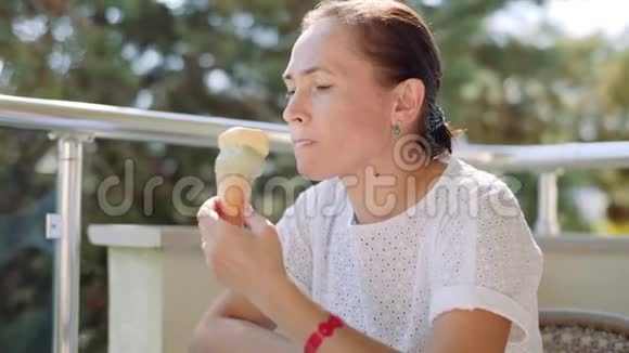 一个穿着白色连衣裙的女人坐在阳台上的玻璃桌前舔冰淇淋4k视频的预览图