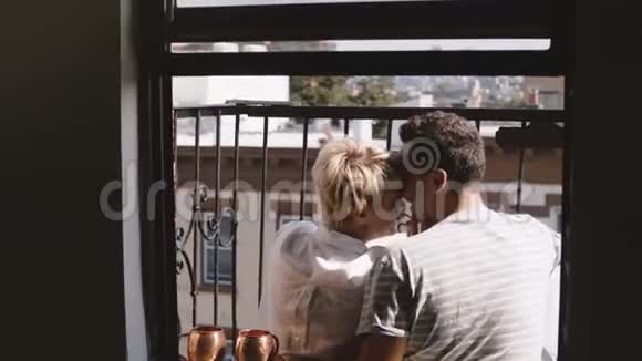 后景幸福浪漫夫妇坐在纽约的一个小公寓阳台上亲吻和拍摄智能手机自拍视频的预览图