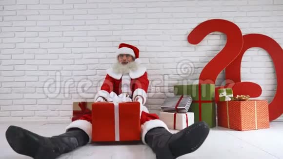 穿圣诞老人服装的快乐老人地板上有礼品盒视频的预览图