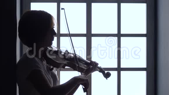 女孩在窗户的背景下拉小提琴剪影视频的预览图