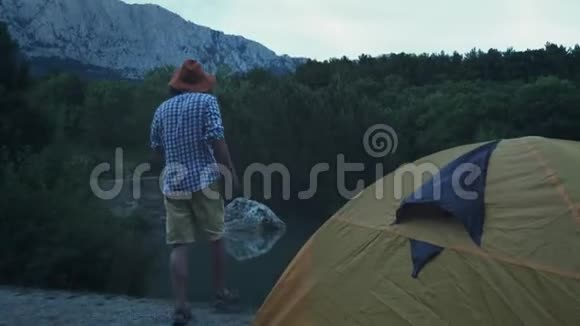 一个年轻的徒步旅行者站在帐篷附近湖边大型森林蜘蛛积极的生活方式穿着格子衬衫视频的预览图