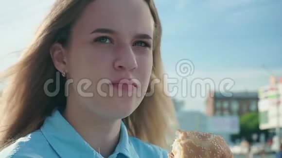 特写镜头拍摄一个女孩在天空背景下吃汉堡视频的预览图