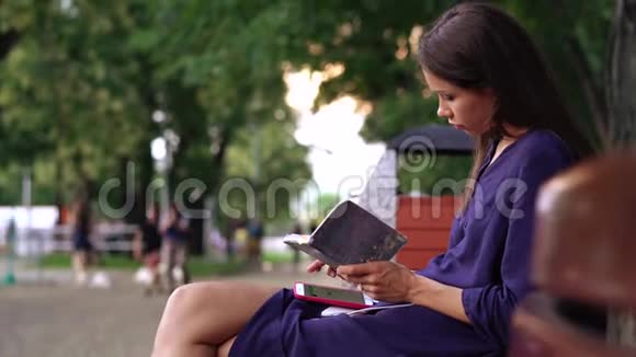 年轻女子穿着随便在公园的长凳上工作视频的预览图