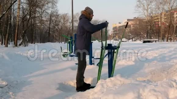 穿着带罩的蓝羽绒服的人在一个冬季城市公园里从事滑雪模拟器侧视视频的预览图