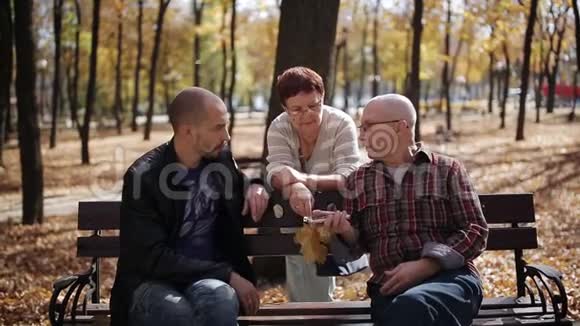 家人在公园散步代之间的联系成年儿子在秋天公园和年迈的父母交谈视频的预览图