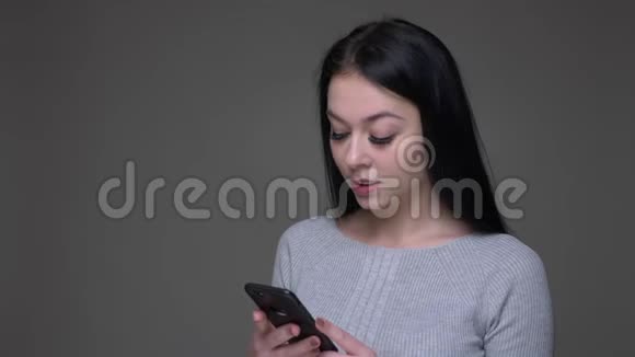 年轻漂亮的黑发白种人女性在手机上发短信背景是灰色的视频的预览图