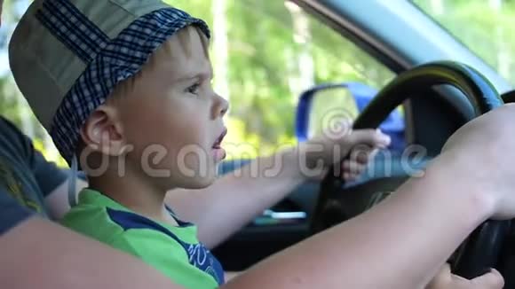 那个男孩坐在车里他坐在爸爸怀里抱着方向盘乡村道路视频的预览图