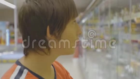 超市里的青少年穿红色t恤的白人少年从货架上的冰箱里挑选奶牛油视频的预览图