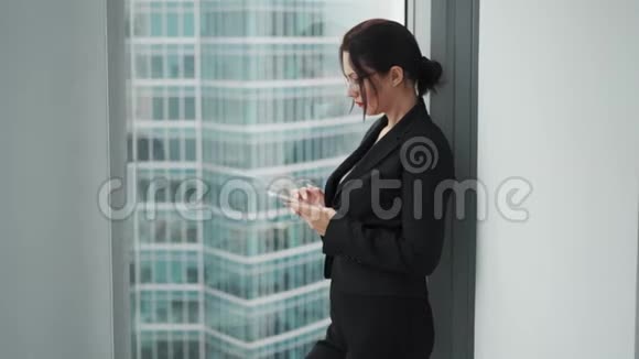 一个手里拿着手机的女商人的画像一个穿着西装的女人站在大窗户旁视频的预览图