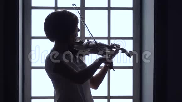 在窗户女孩拉小提琴的背景下剪影视频的预览图
