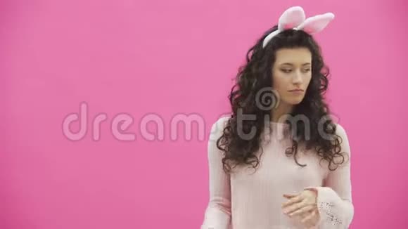 美丽的年轻女孩站在粉红色的背景上在这期间头上有兔子的耳朵表演兔子视频的预览图