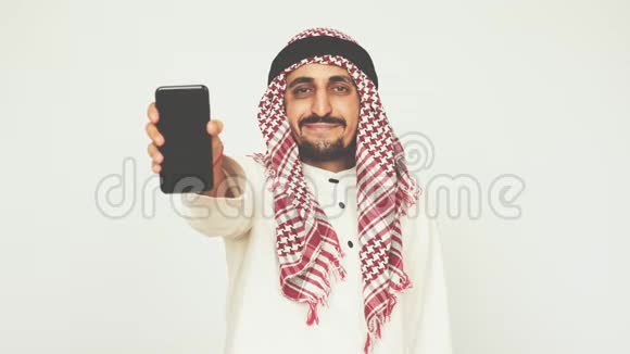 穿着民族服装微笑的阿拉伯人展示了智能手机和广泛的微笑一个男人展示一部现代手机商业和办公室阿拉伯视频的预览图