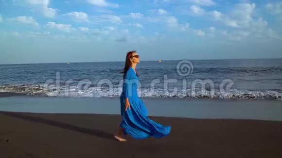穿着蓝色裙子的女人沿着黑色的火山海滩奔跑视频的预览图