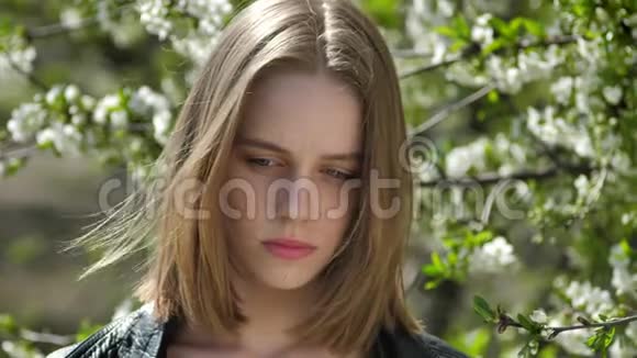 一个年轻悲伤的女孩在公园里看着夏天的白天想着概念在背景上绽放树视频的预览图