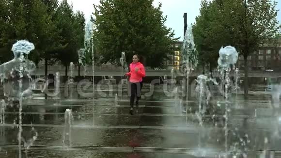 在城市公园喷泉附近的雨中奔跑的年轻混血运动女子超级慢镜头视频的预览图