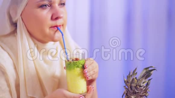 一位年轻的穆斯林妇女戴着浅色围巾喝着水果奶昔微笑着视频的预览图