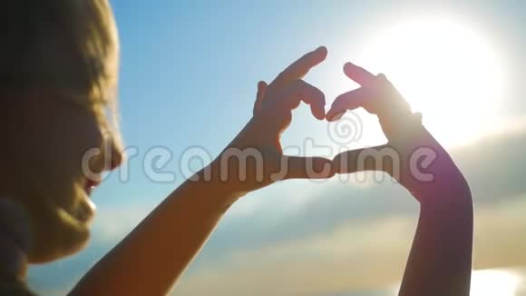 手形成心形与日落剪影海洋的阳光透过心形的女性手照耀爱大自然视频的预览图