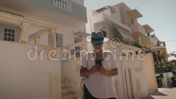 戴帽子戴太阳镜的女孩自拍那个女孩拿着电话在白色建筑的背景下视频的预览图