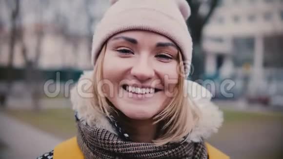 特写生活方式肖像年轻美丽的白种人女孩戴着冬帽微笑快乐在寒冷的日子看着相机视频的预览图