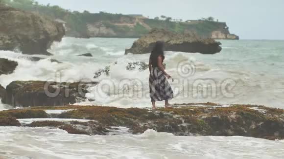 一个年轻的印度尼西亚女孩很高兴在巴厘岛的岩石海岸上掀起巨浪视频的预览图