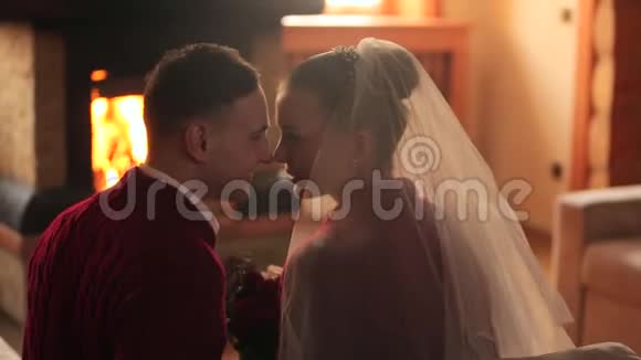 热恋中的新婚夫妇穿着红色毛衣在壁炉边热身新郎新娘在温暖的炉火下放松亲吻视频的预览图