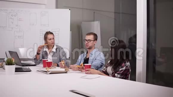 年轻的白种人同事午休时一起在办公室吃披萨笑说话玩得开心工作人员视频的预览图