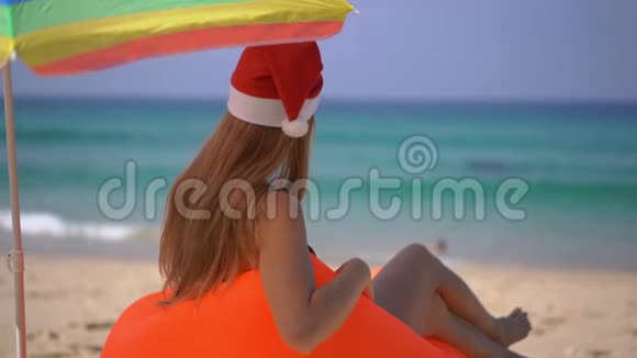 一位戴着圣诞帽在伞下充气沙发上放松的年轻女子的超慢动作镜头视频的预览图