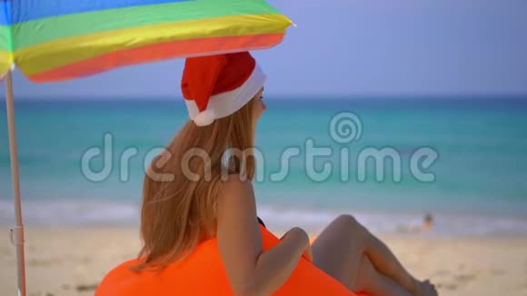 一位戴着圣诞帽的年轻女子在一把伞下放松躺在充气沙发上的超慢动作镜头视频的预览图