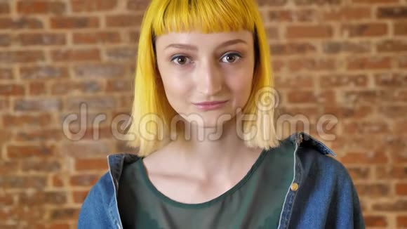 年轻迷人的女人黄发看着相机站在砖背景附近微笑着积极向上视频的预览图