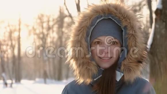 特写的女人脸在毛皮罩里看着镜头在冬天阳光明媚的公园里微笑就在视频里视频的预览图