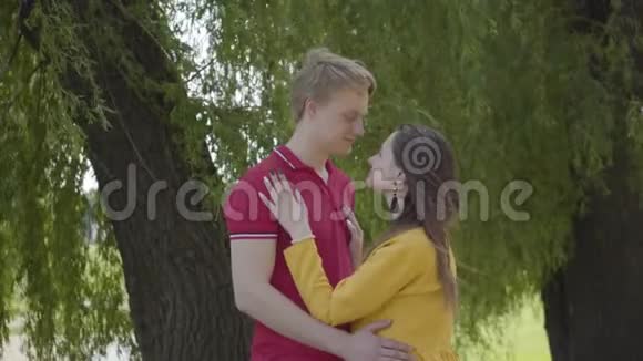 幸福的白种人夫妇在绿泉公园的背景下温柔地拥抱和微笑年轻日期视频的预览图