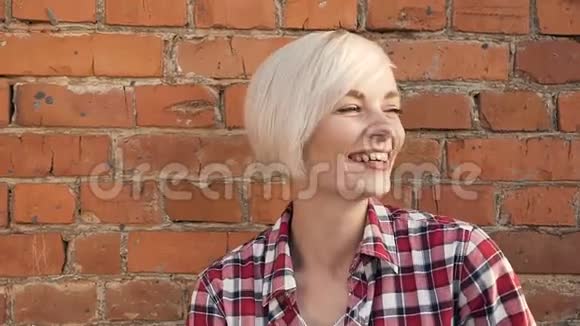 时髦的金发女孩模特站在红砖墙边年轻美丽的白种人金发女郎微笑的肖像视频的预览图