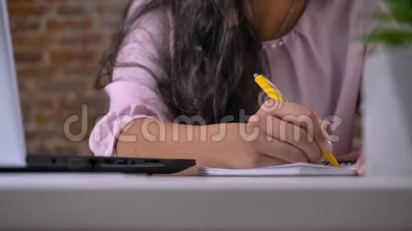 年轻忙碌的女孩在阁楼办公室里用笔记本电脑工作打字在笔记本上写纸条在砖墙上写字视频的预览图